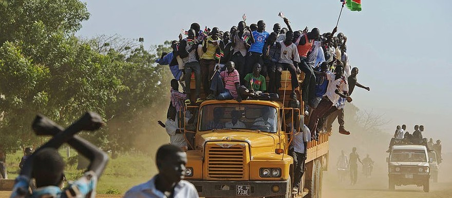 Residents hang from a bus and hold a South Sudanese flag in the disputed Abyei region of Sudan. [Photo: ALI NGETHI/AFP via Getty Images]